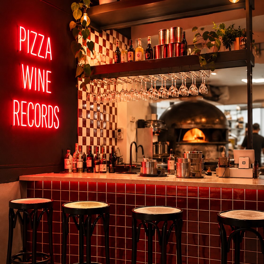 The full Bolla bar: red tiled counter and stools, checkerboard wall, pizza oven and neon in the room