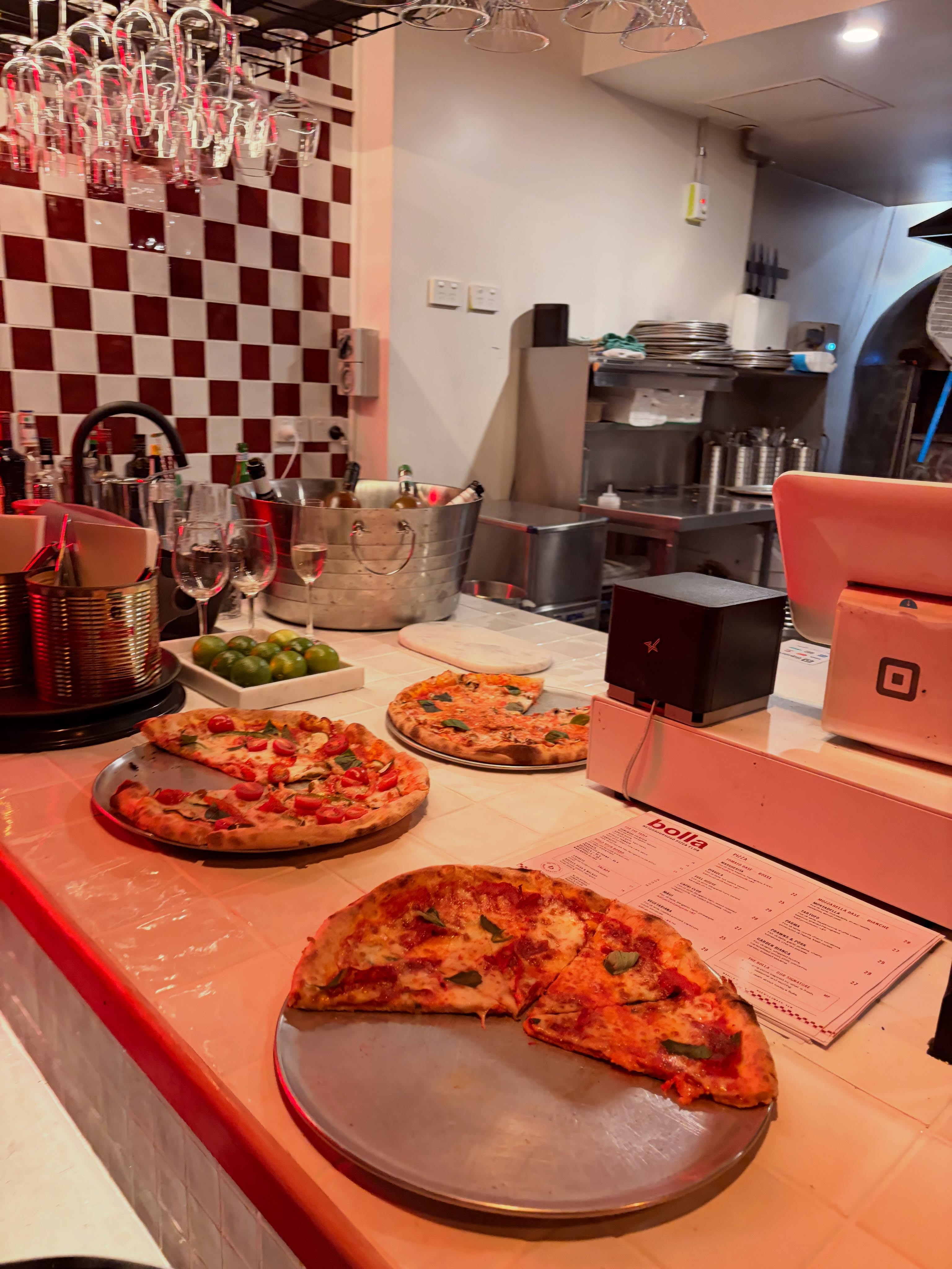 Pizzas on Bolla's real service counter, with checkerboard tiles and the oven in view